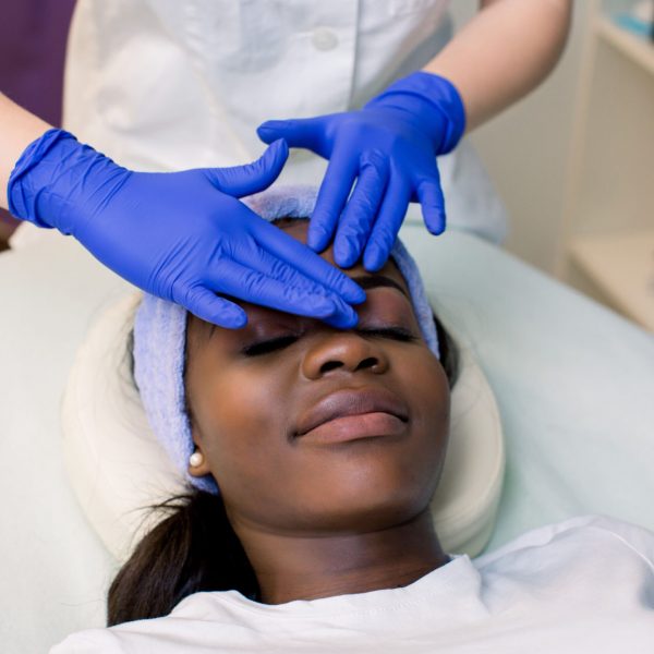 relaxed-young-african-woman-receiving-forehead-massage-spa-woman-massagist-blue-rubber-gloves-performing-facial-massage-spa-massage-concept-scaled.jpg